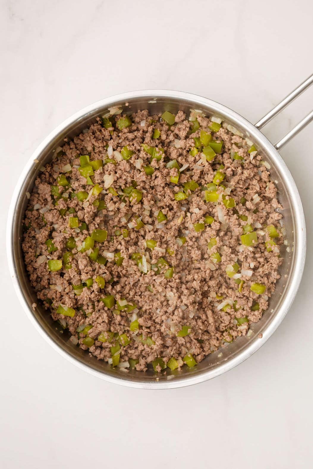 ground beef cooked with chopped onions and green bell pepper in a stainless steel pan. 