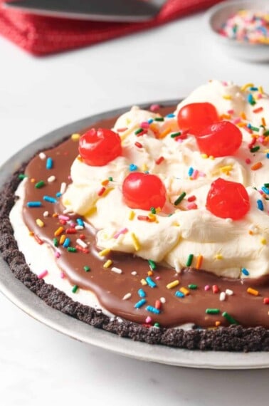 An Oreo crust ice cream pie topped with whipped cream and cherries.