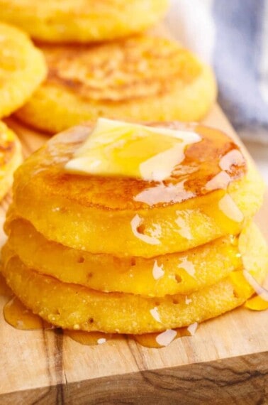A stack of cornbread fritters topped with butter and honey.