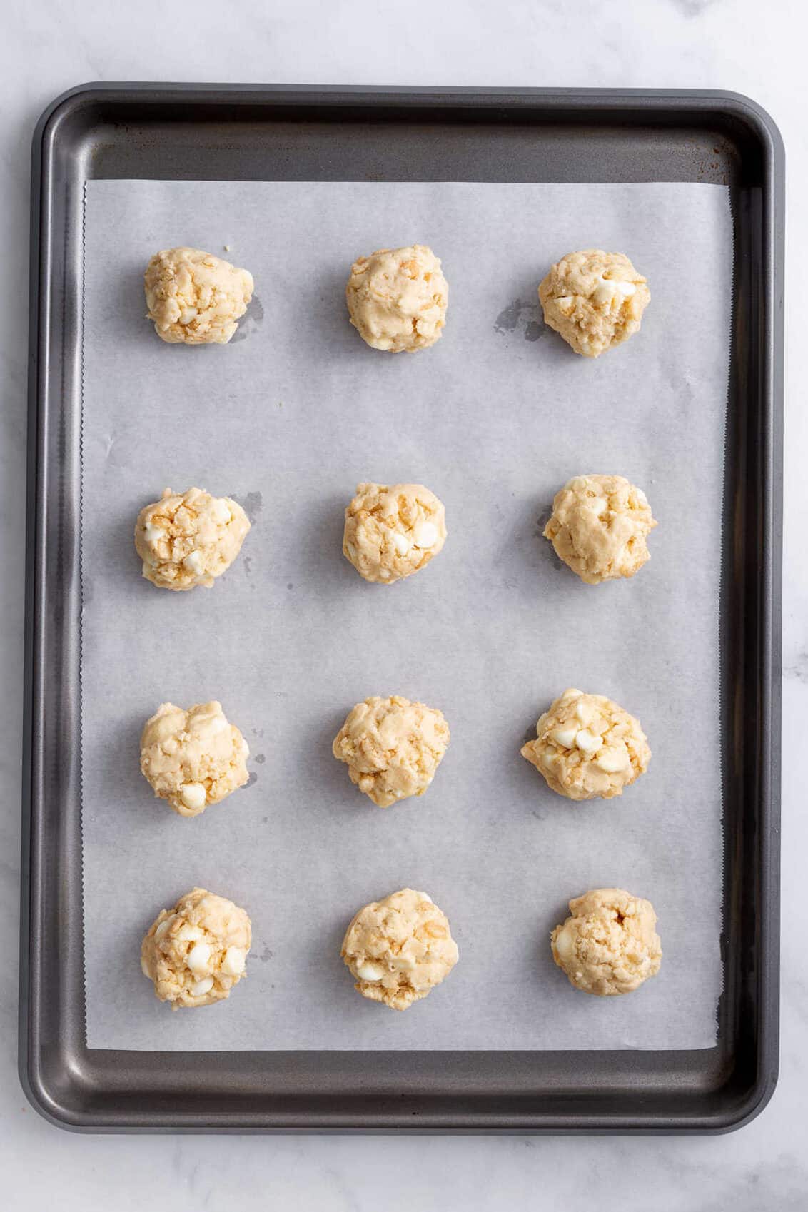 twelve rice krispies cookie dough ball prepped and arranged on a parchment-lined baking sheet.