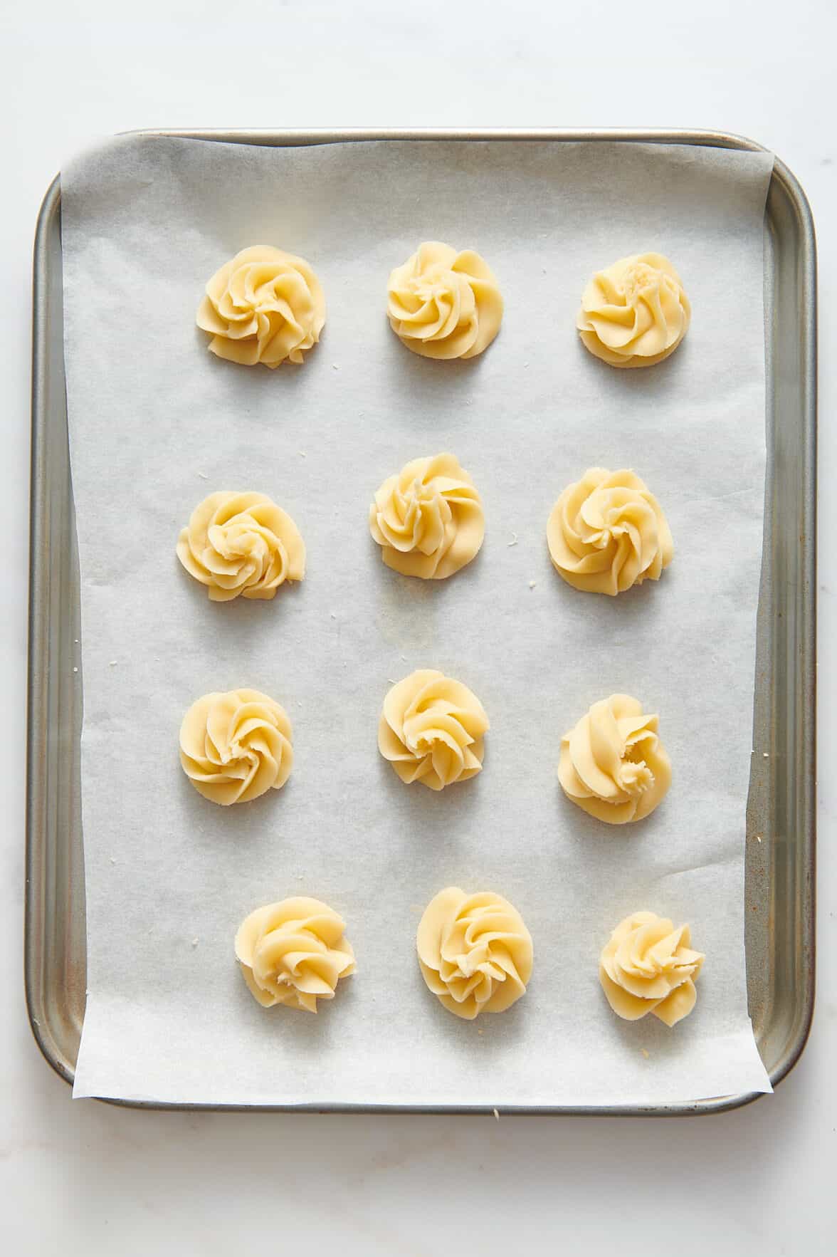 12 unbaked christmas butter cookies sitting on a parchment-lined baking tray. 