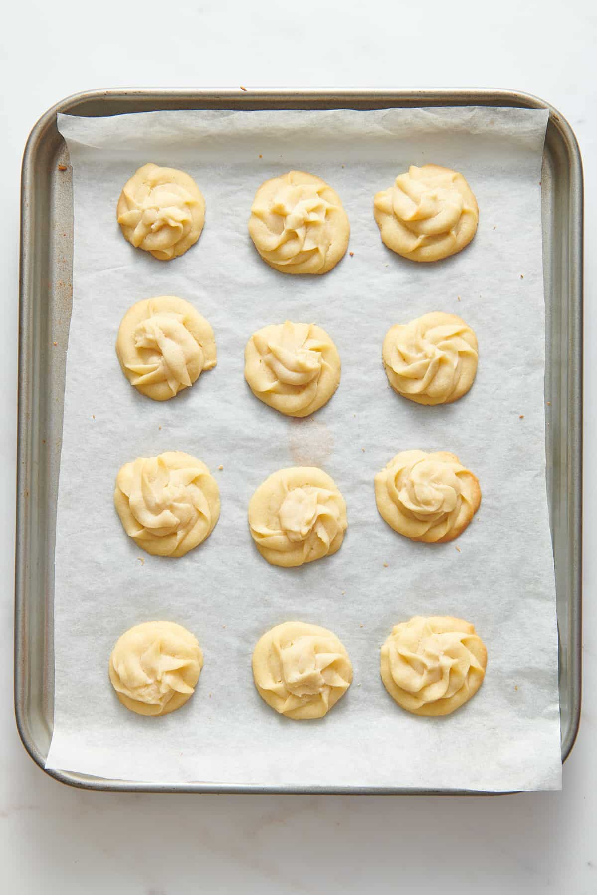 12 christmas butter cookies baked and sitting on a parchment-lined baking tray. 