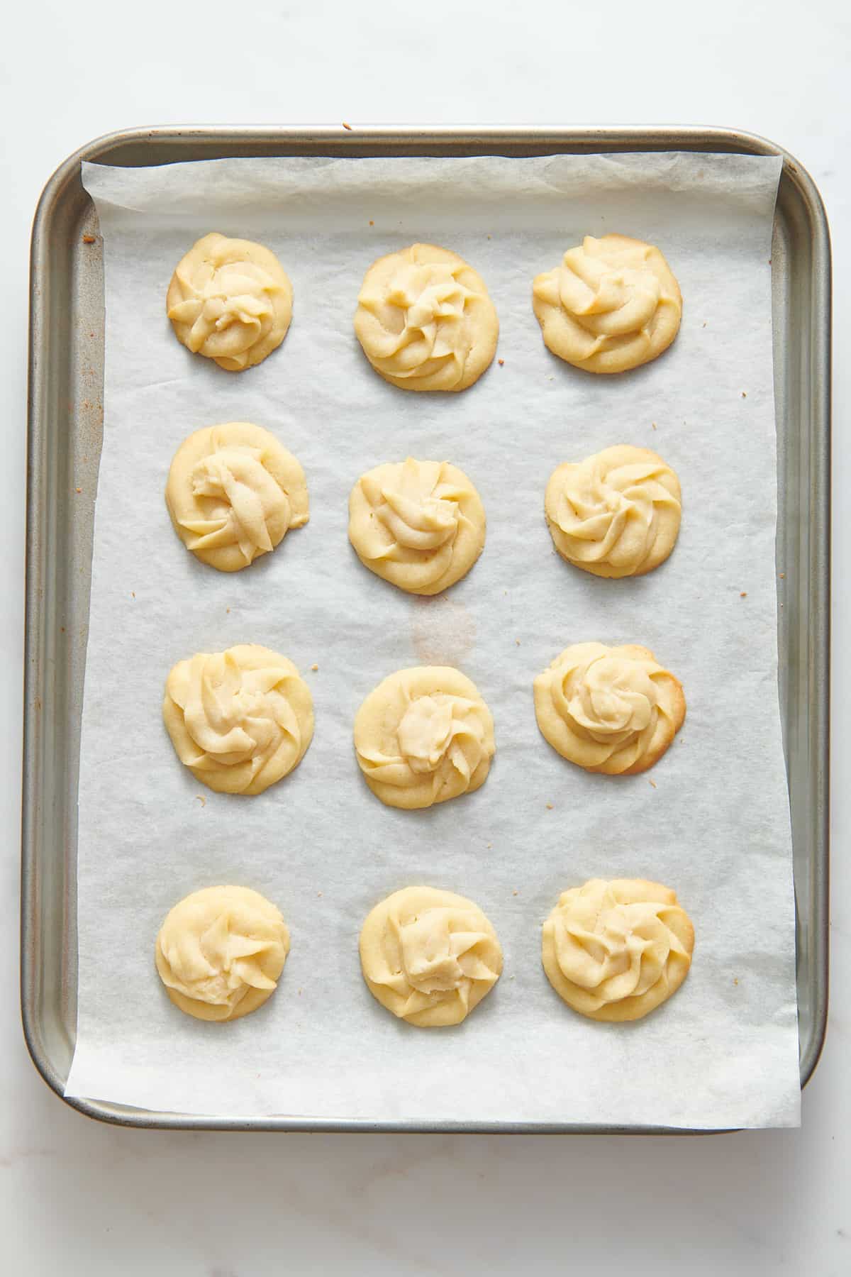 12 christmas butter cookies baked and sitting on a parchment-lined baking tray.