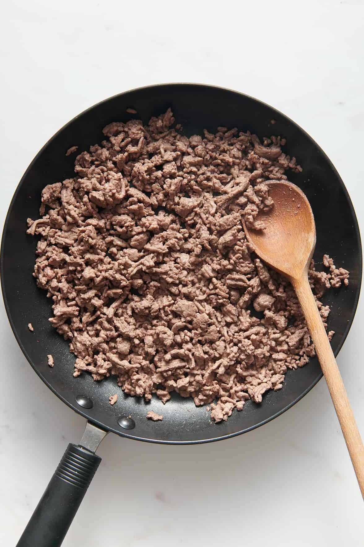 cooked ground beef in a skillet with a wooden spoon. 