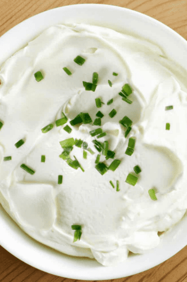 Close up image of a bowl of sour cream topped with herbs.