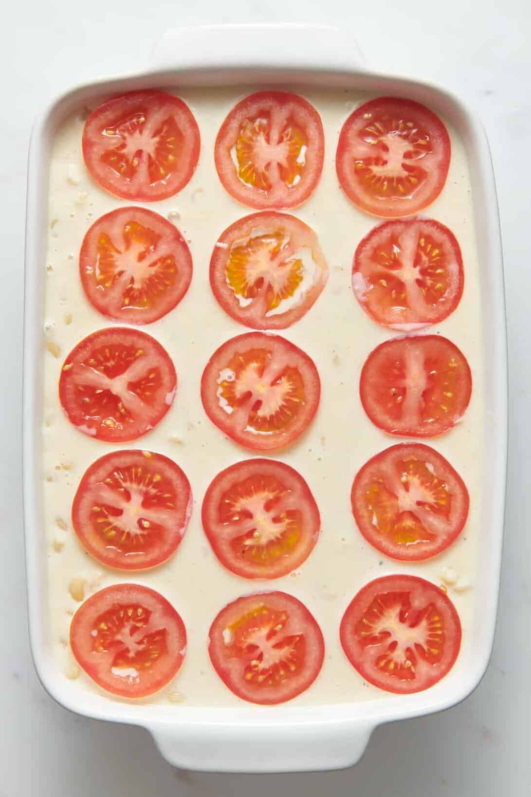 sliced fresh tomatoes layered on top of ina mac and cheese in a 9x13 casserole dish. 