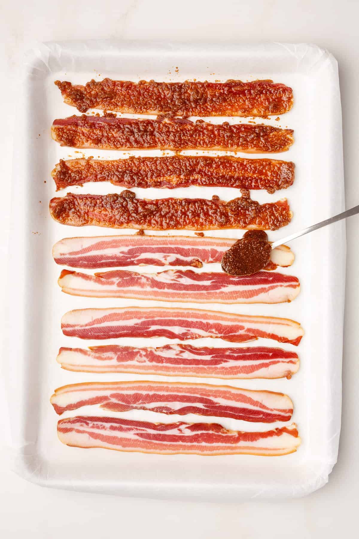 4 prepared million dollar bacon strips and 6 strips of bacon sitting on a parchment-lined baking sheet. 