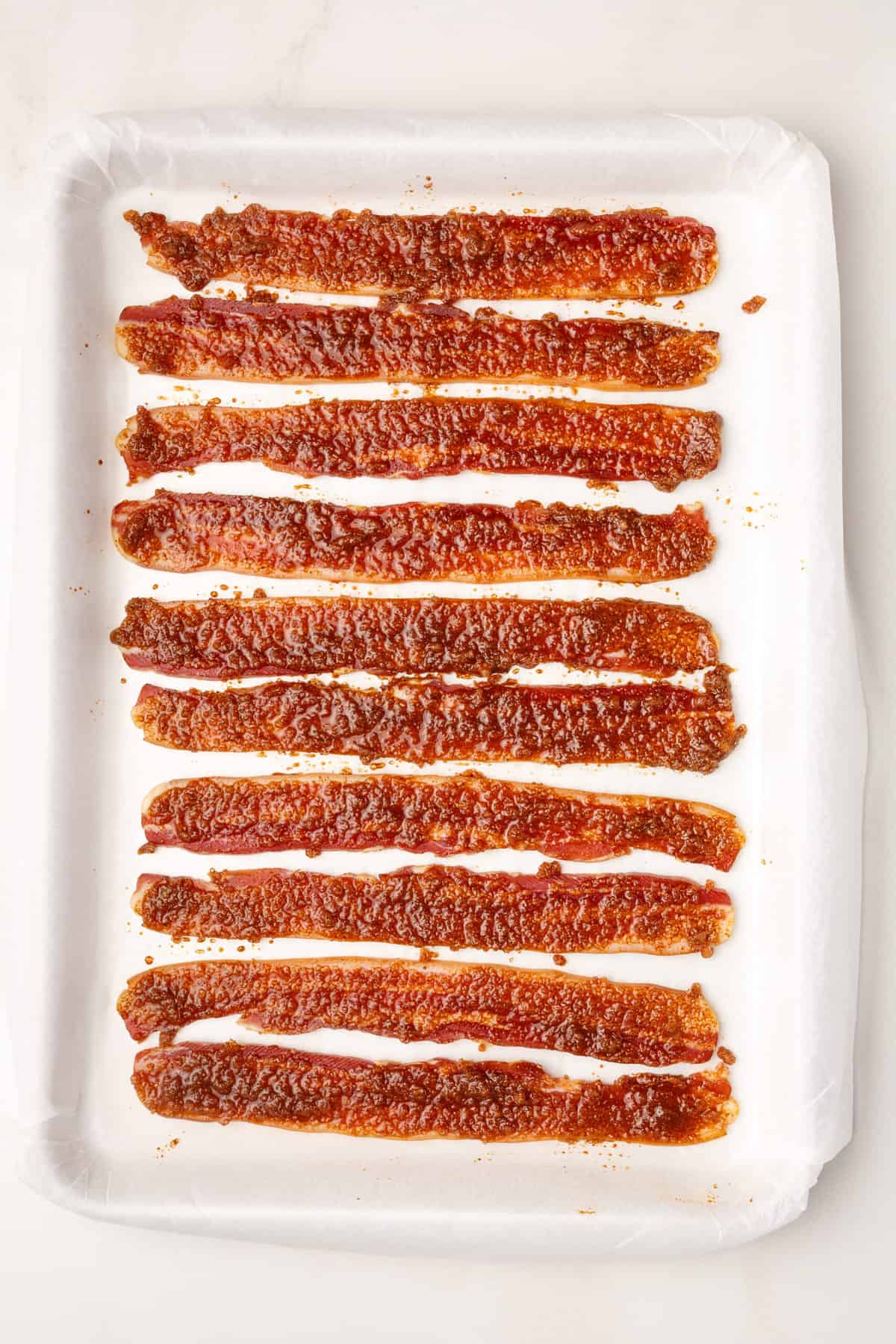 10 prepared million dollar bacon strips sitting on a parchment-lined baking sheet. 