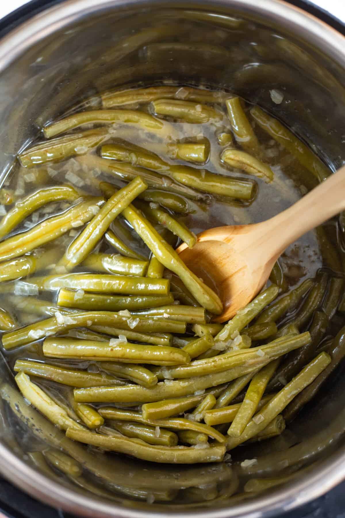 Green beans in Instant Pot with wooden spoon.