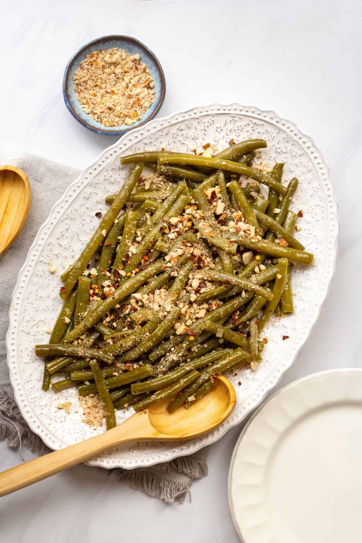 top down image of a white decorative oval plate with a pile of instant pot green beans topped with crushed almonds and red pepper flakes. 