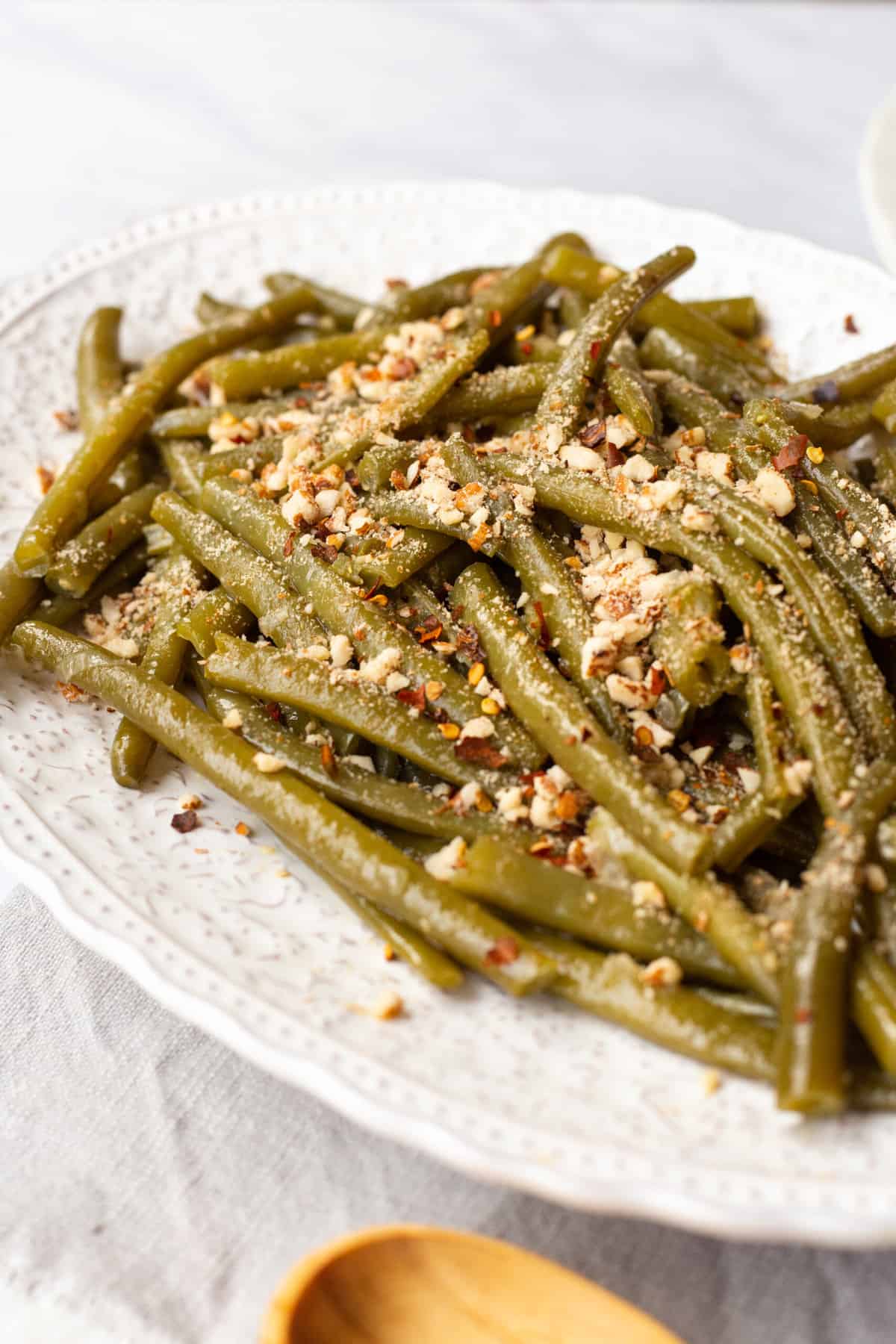 close up image of a plate of instant pot green beans topped with crushed almonds and red pepper flakes. 