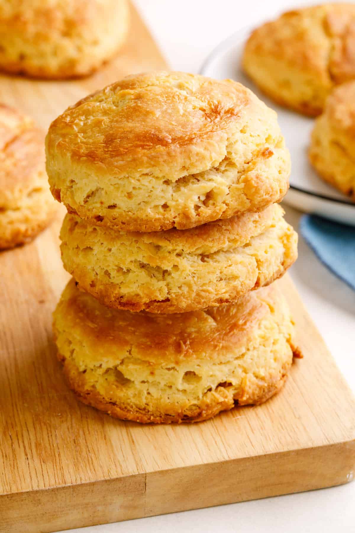 stack of three sour cream biscuits sitting on a wood cutting board. 