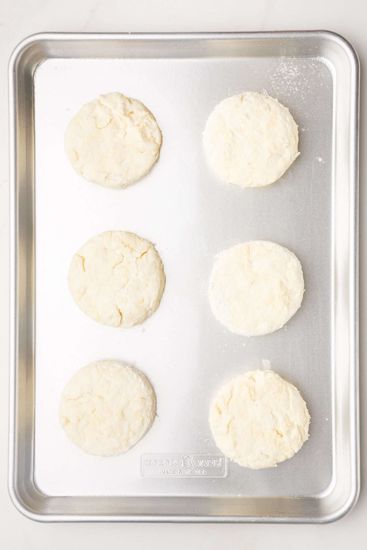 six sour cream biscuits prepared on a baking sheet. 