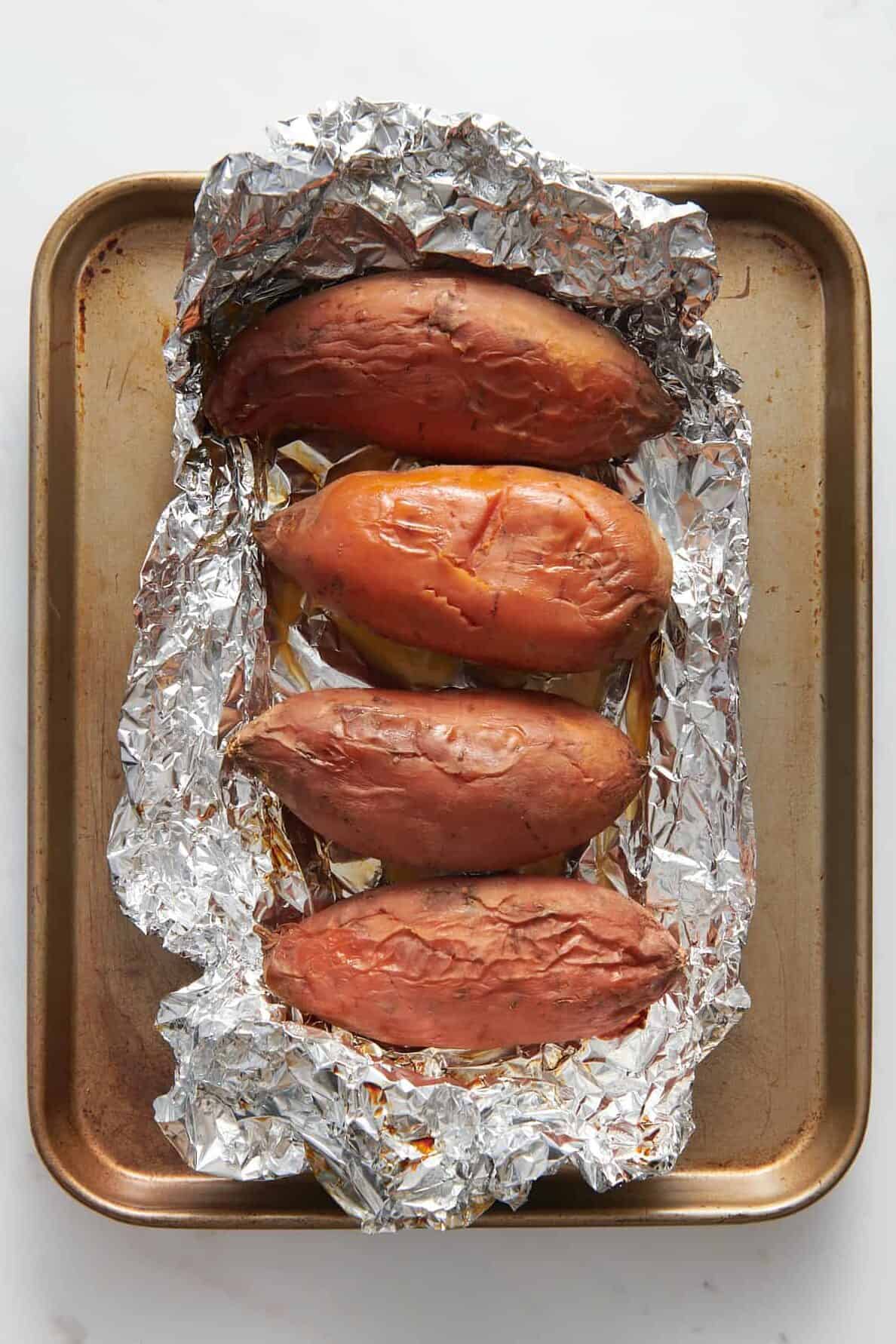 four roasted sweet potato unwrapped from foil and sitting on a baking tray. 