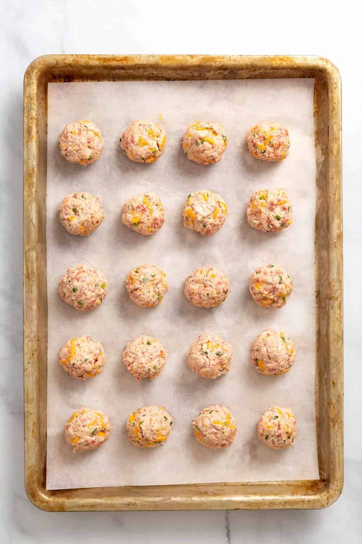 20 unbaked cream cheese sausage balls sitting on a parchment-lined baking sheet.