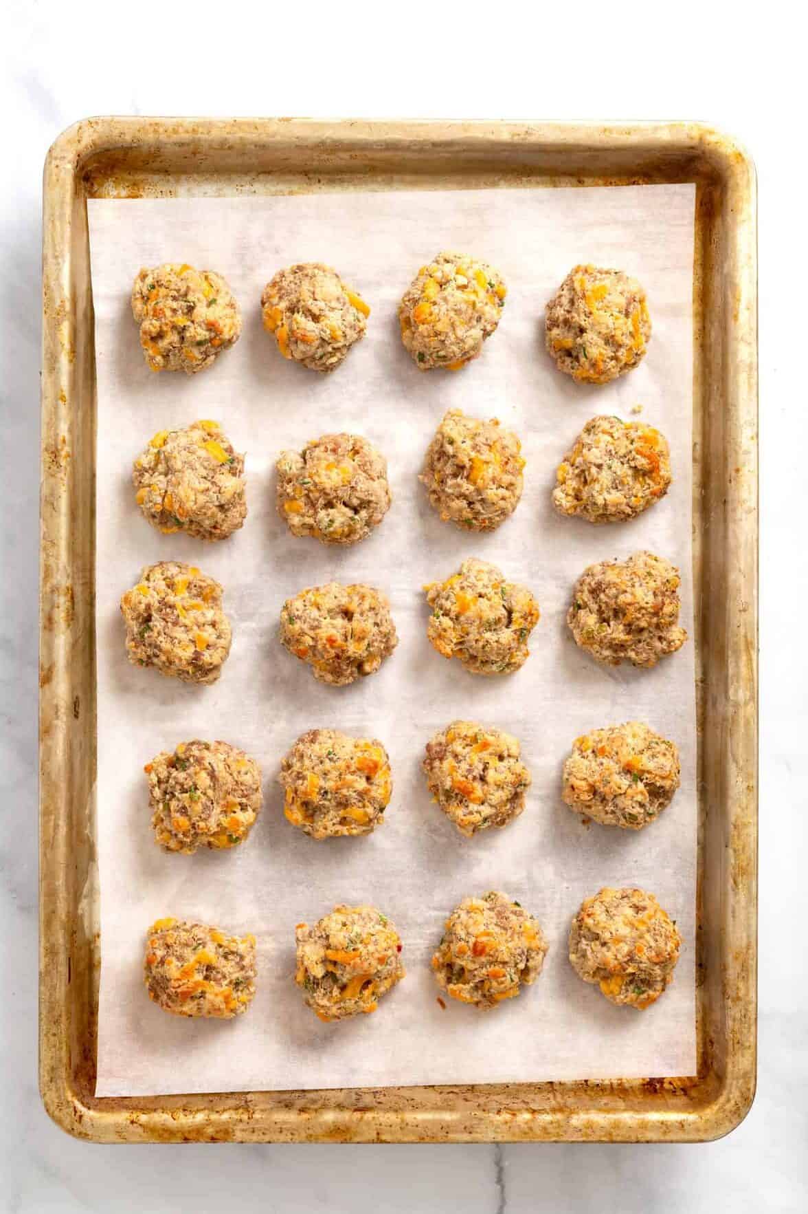 20 baked cream cheese sausage balls sitting on a parchment-lined baking sheet.