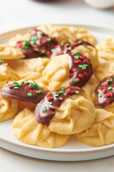 A plate of Christmas butter cookies, some topped with chocolate and sprinkles.