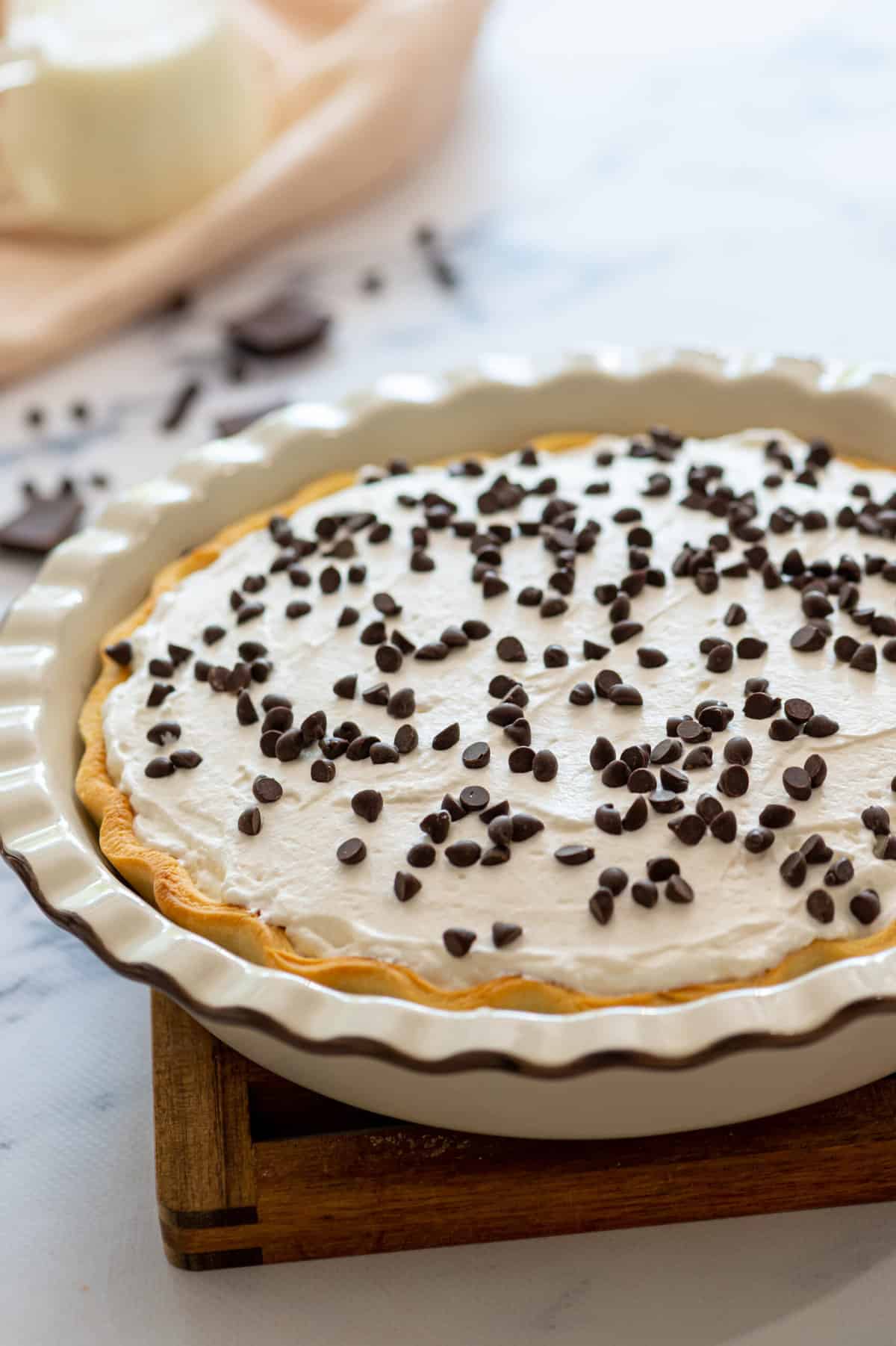 chocolate cream pie sitting in a pie dish on top of a wooden cutting board. 