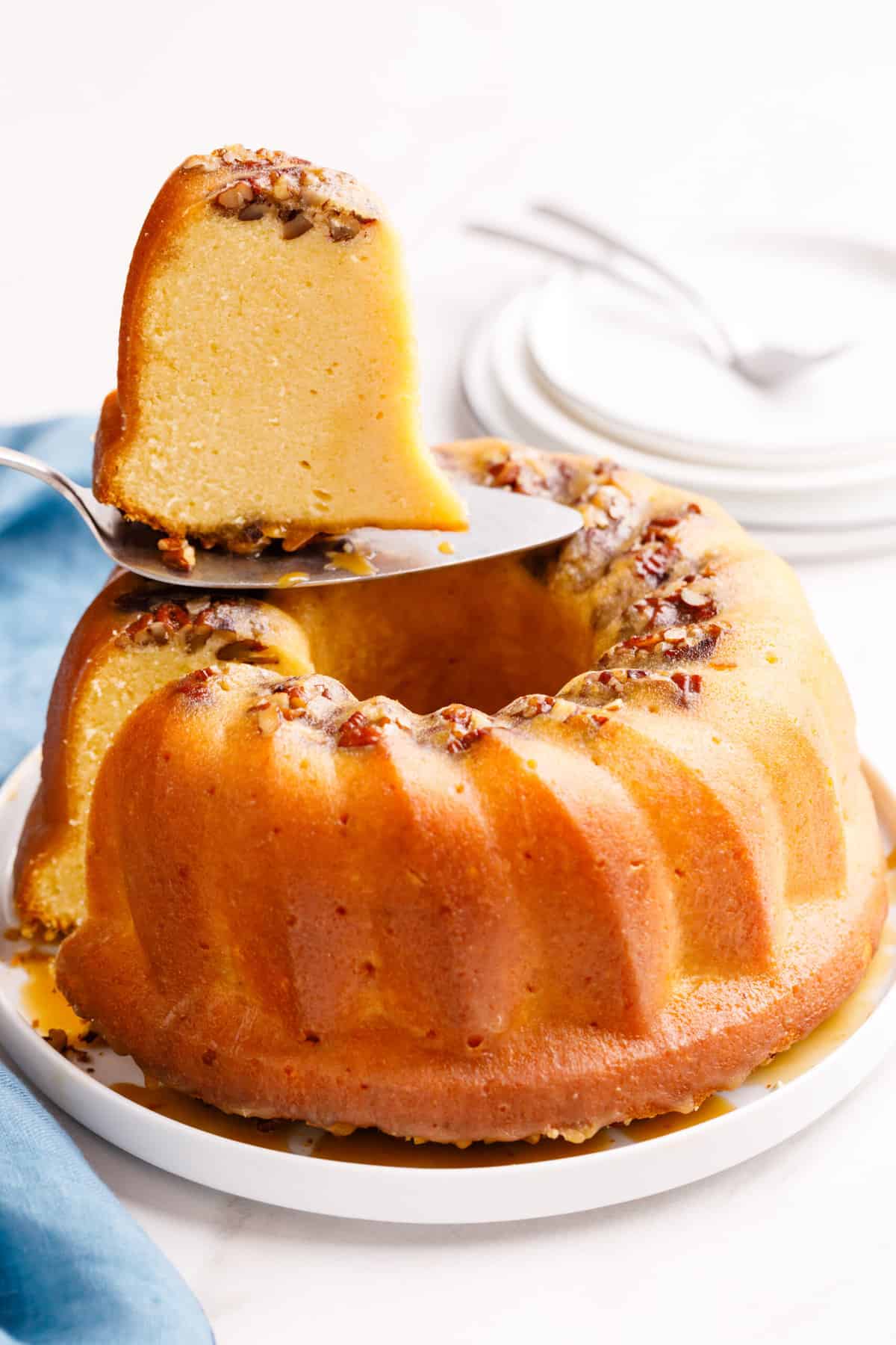 slice of cake mix rum bundt cake sitting on a metal cake spatula with the whole cake sitting on a white round plate. 