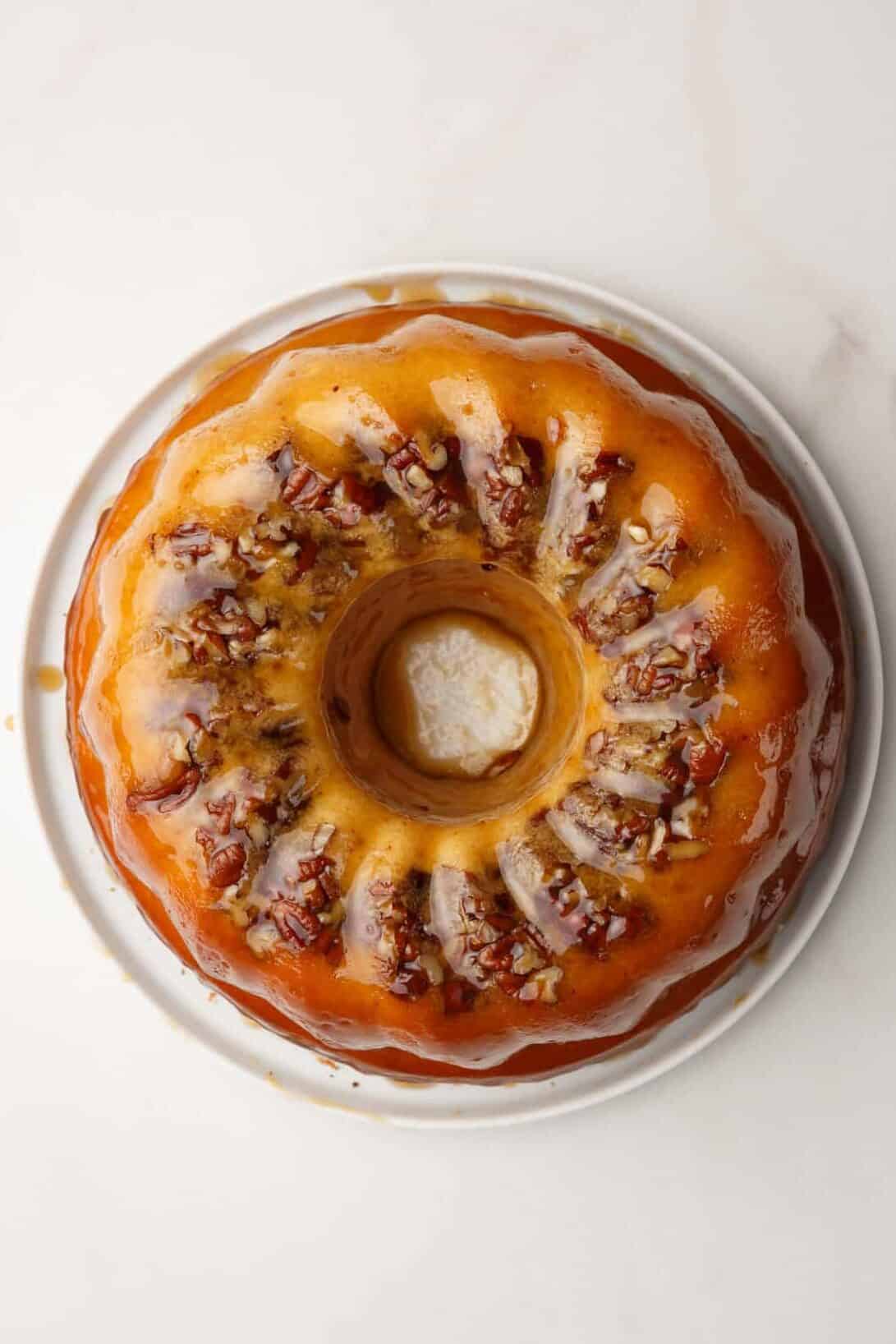 cake mix run bundt cake with pecans sitting on a white round plate topped with glaze.