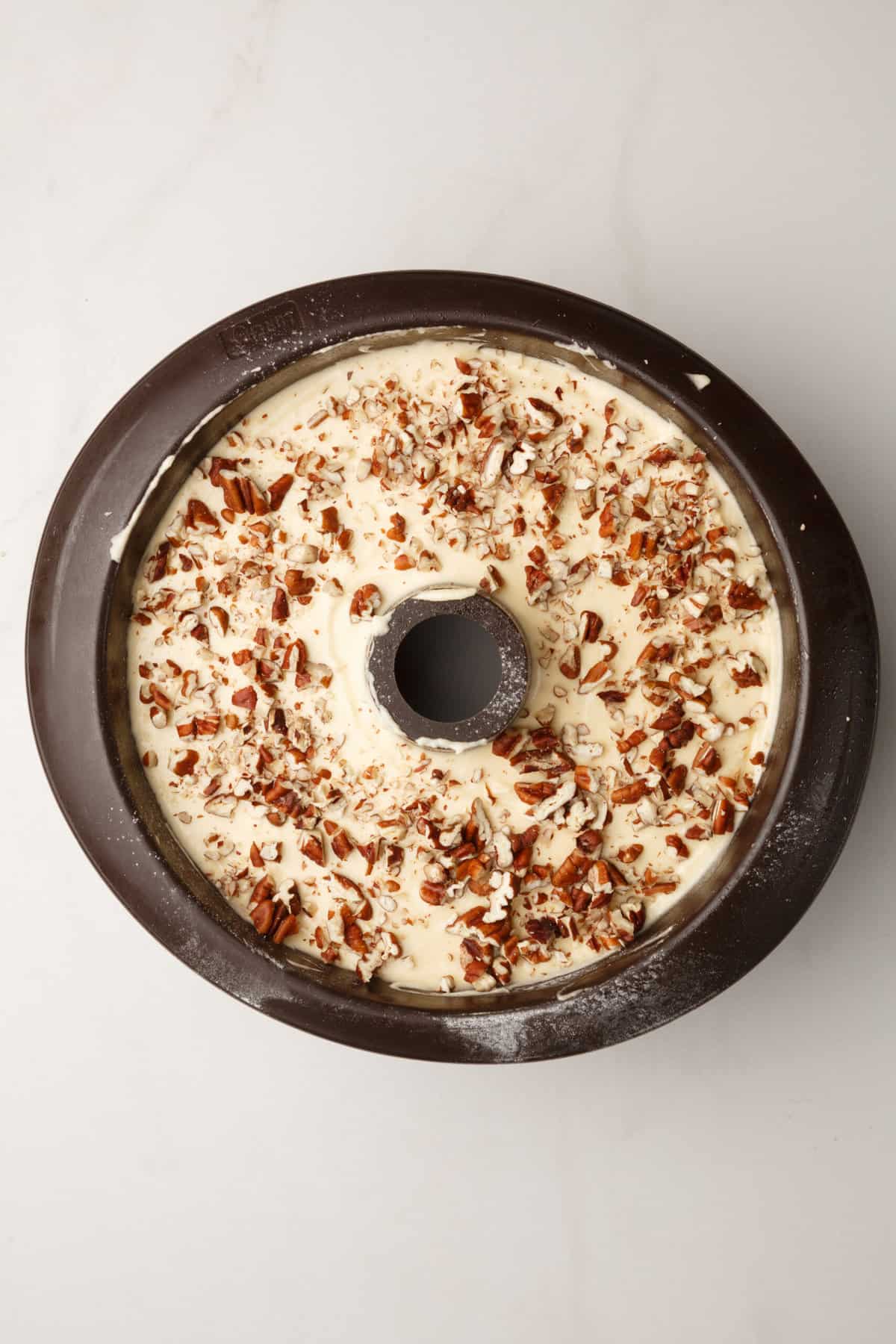 bundt cake tin with cake batter topped with chopped pecans.  