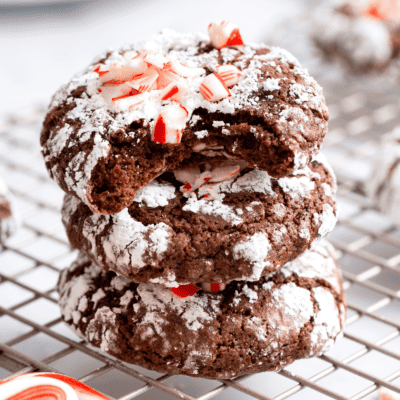 Three chocolate mint crinkle cookies stacked on top of each other with the top cookie missing a bite.