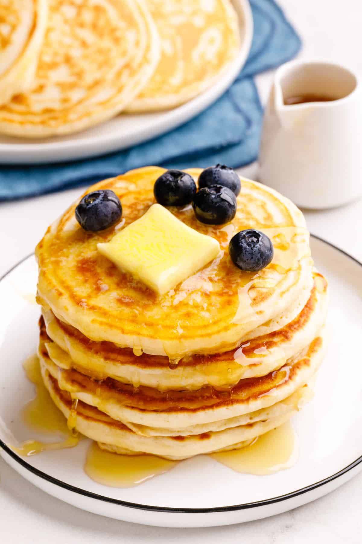 stack of four classic bisquick pancakes topped with a slab of butter, fresh blueberries and maple syrup. 