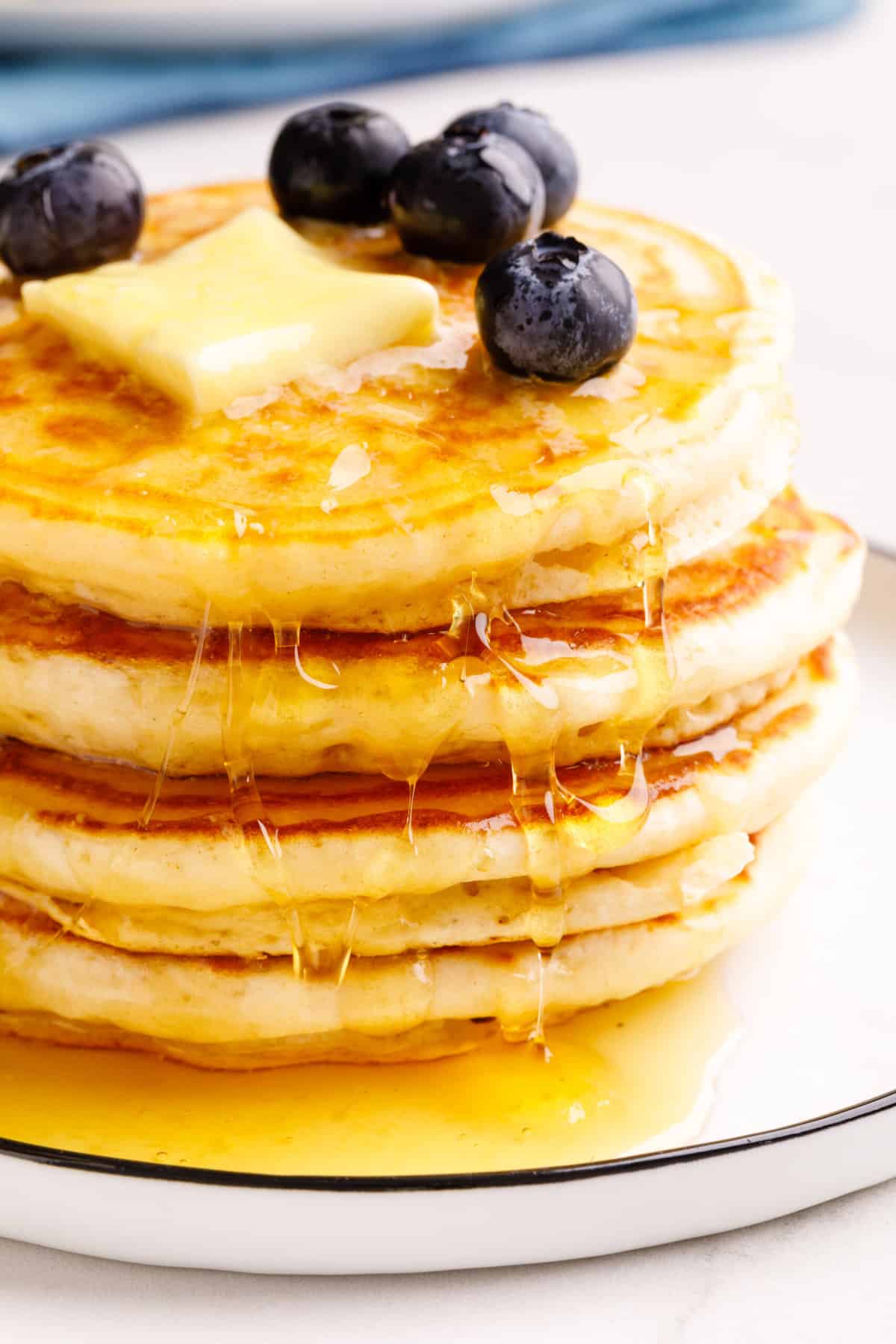 close up image of classic bisquick pancakes topped with a slab of butter, fresh blueberries and maple syrup. 