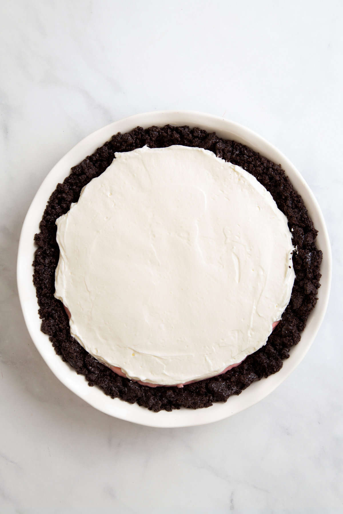 top down image of oreo pie crust with red cool whip filling topped with regular cool whip filling. 