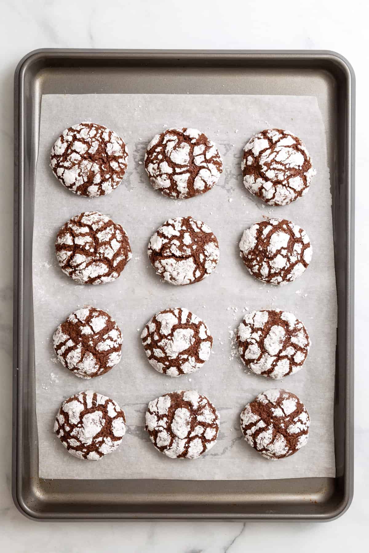 parchment-lined baking sheet with twelve chocolate mint crinkle cookies. 