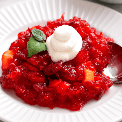A bowl of cranberry jello salad topped with whipped cream.