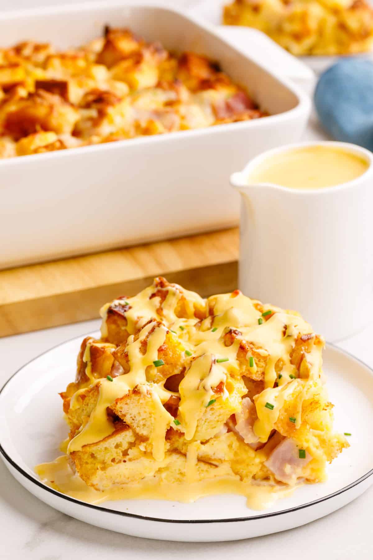 serving of eggs benedict casserole topped with hollandaise sauce served on a white round plate. 