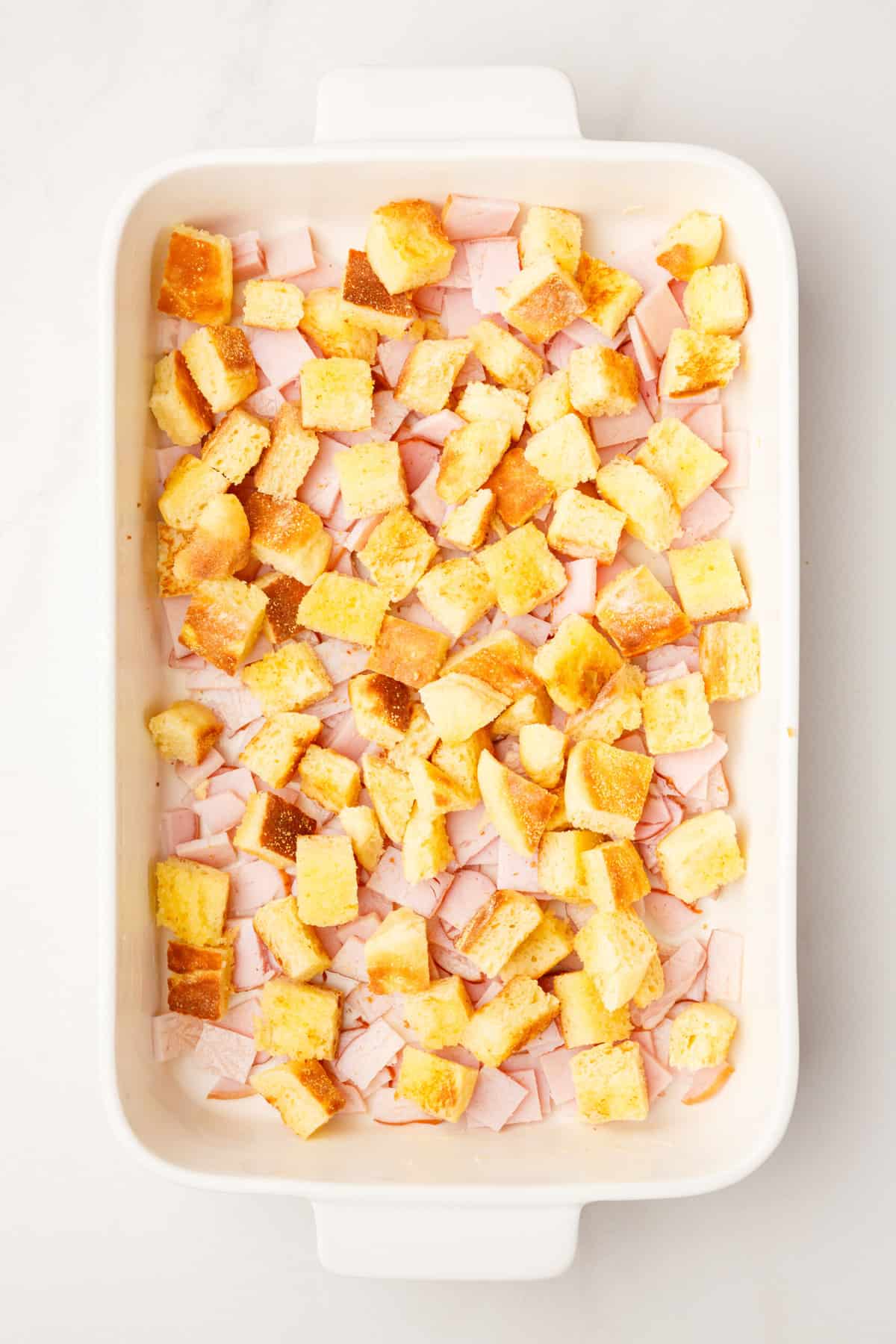 chopped canadian bacon pieces and the cubed english muffin pieces layering the bottom of a 9x13 casserole dish. 