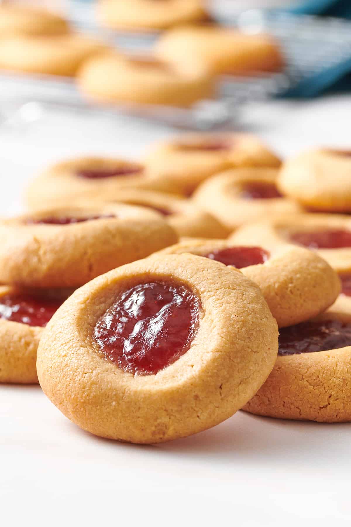 close up image of a pile of strawberry jam filled peanut butter thumbprint cookies. 