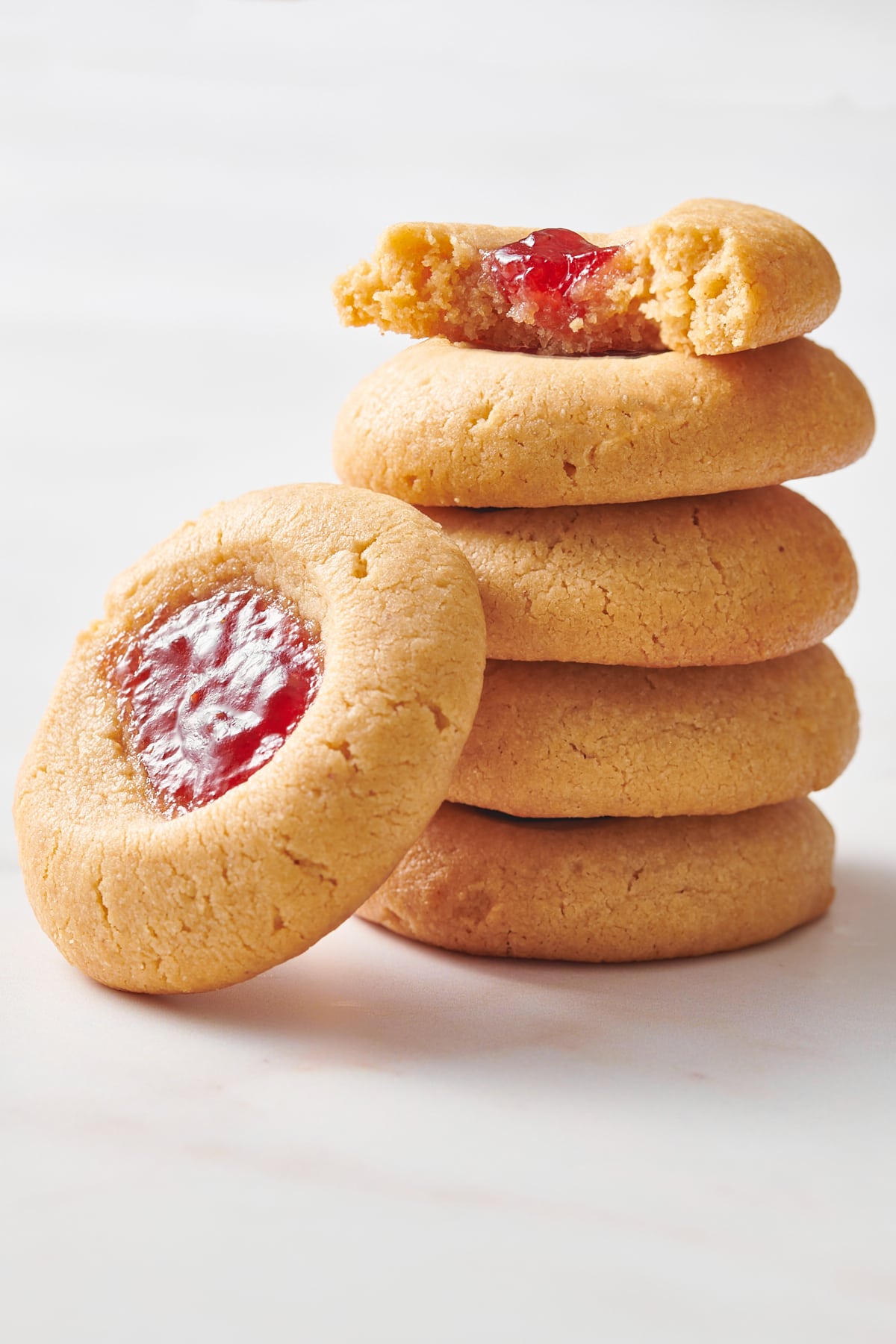 stack of four peanut butter thumbprint cookies with one cookie leaning on the stack. 