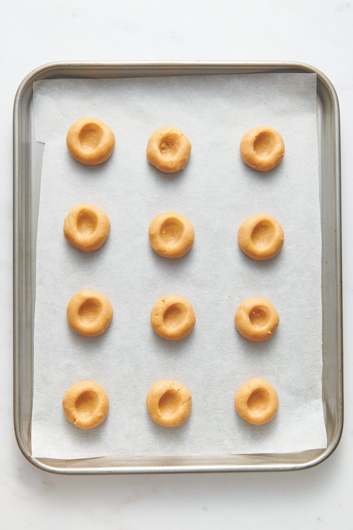 peanut butter thumbprint cookies prepped on a parchment-lined baking tray. 