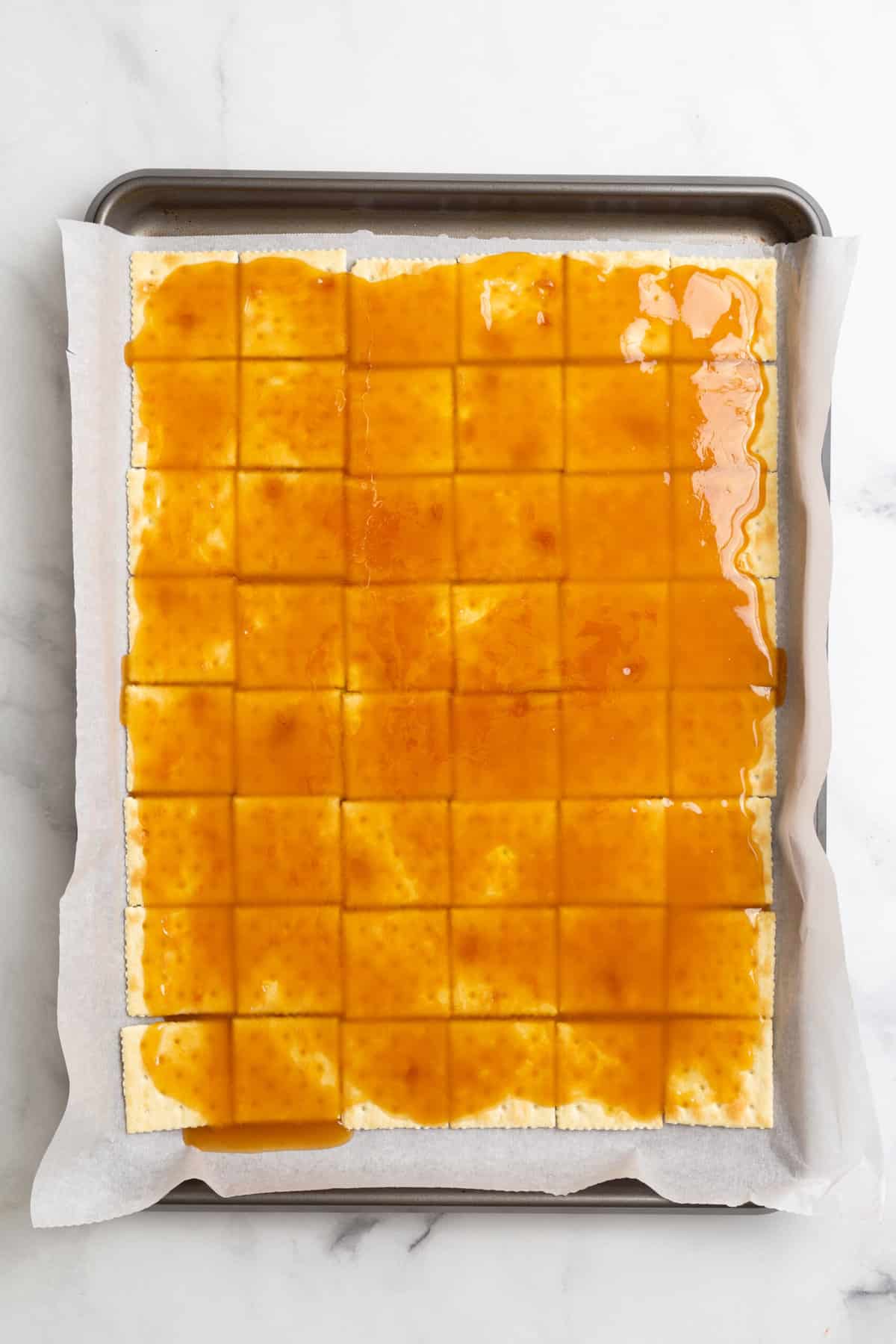 parchment-lined baking sheet with saltines arranged at the bottom and layered with caramel on top. 