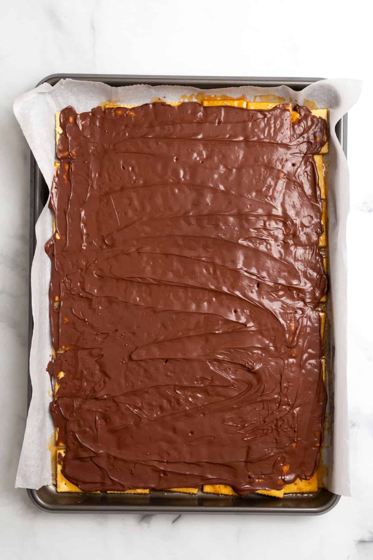 parchment-lined baking sheet with saltines arranged at the bottom and layered with caramel and melted chocolate on top. 