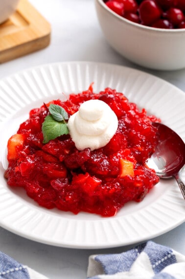 A bowl of cranberry jello salad topped with whipped cream.