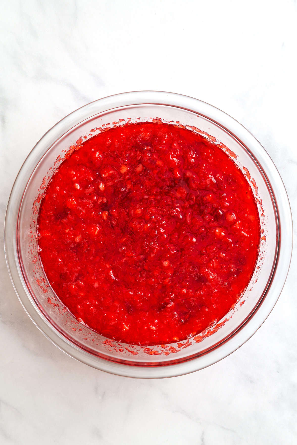 raspberry jello mix with water and crushed pineapple in a large glass mixing bowl. 