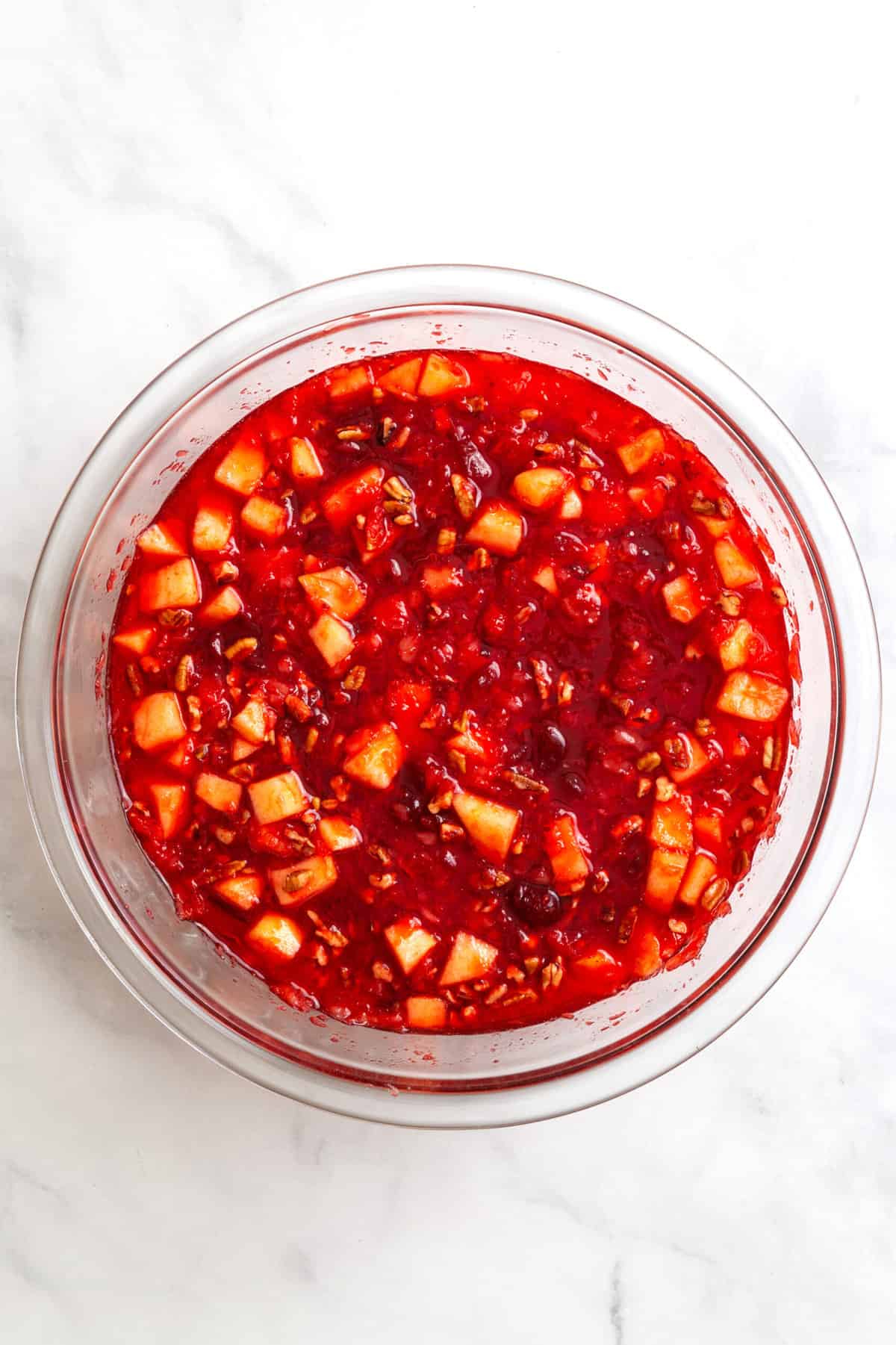 raspberry jello mix with water and crushed pineapple and cranberry sauce in a large glass mixing bowl. 