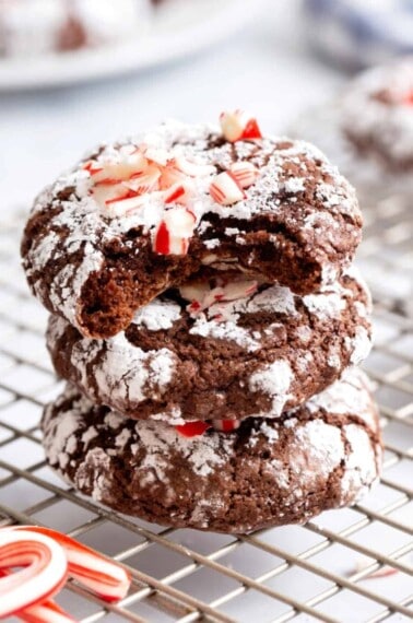 Three chocolate mint crinkle cookies stacked on top of each other, the top cookie missing a bite.
