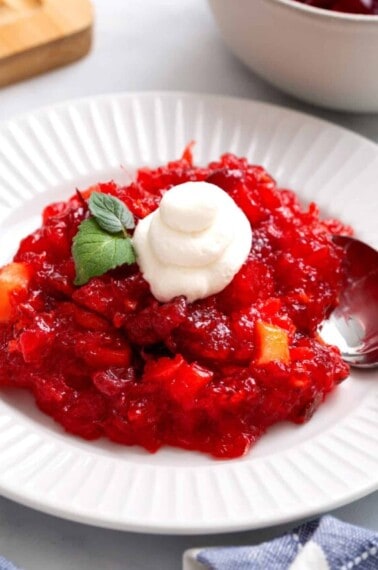 A bowl of cranberry jello salad topped with whipped cream.