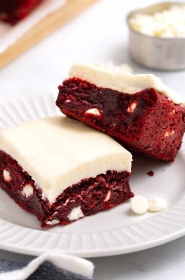 Two red velvet brownies with cream cheese frosting on a plate.