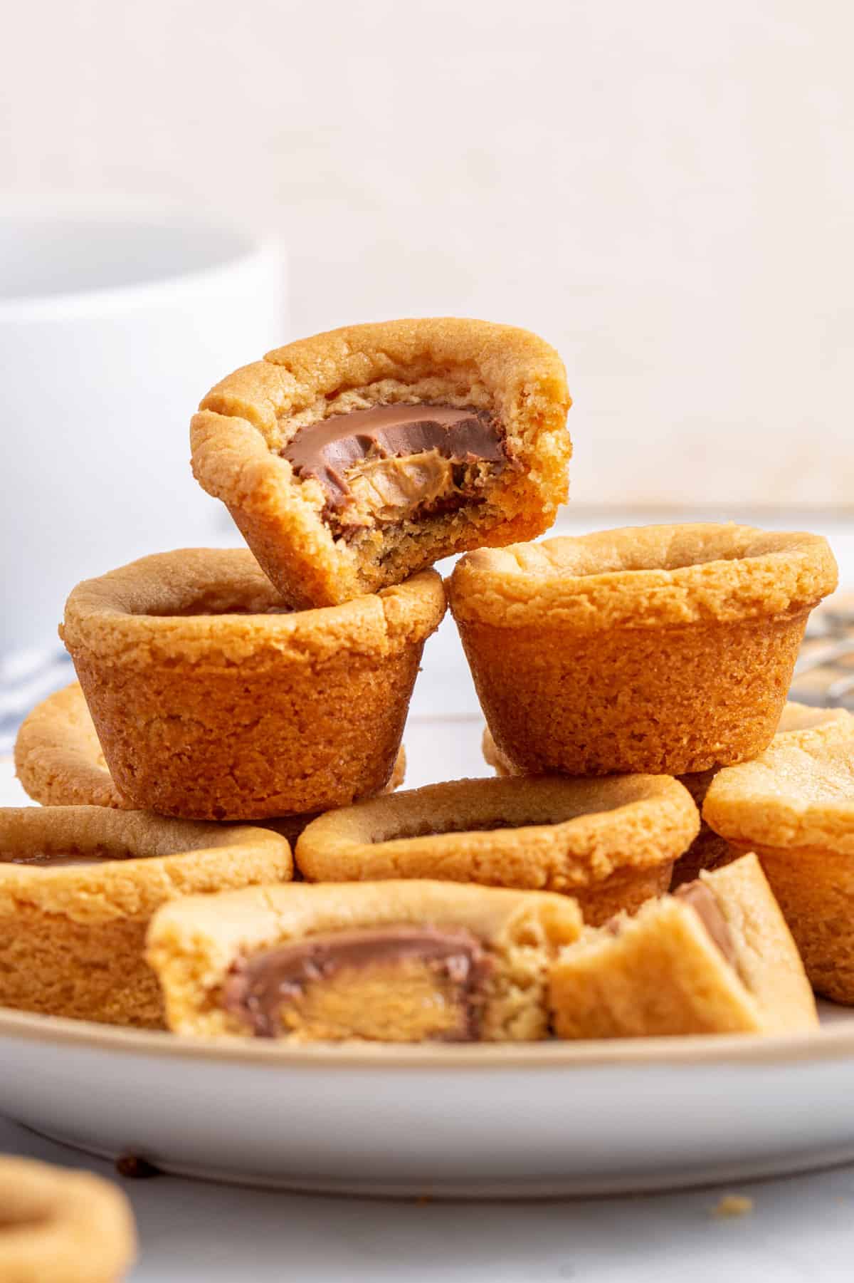 stack of peanut butter cookie cups sitting on a plate with one taken a bite out of. 
