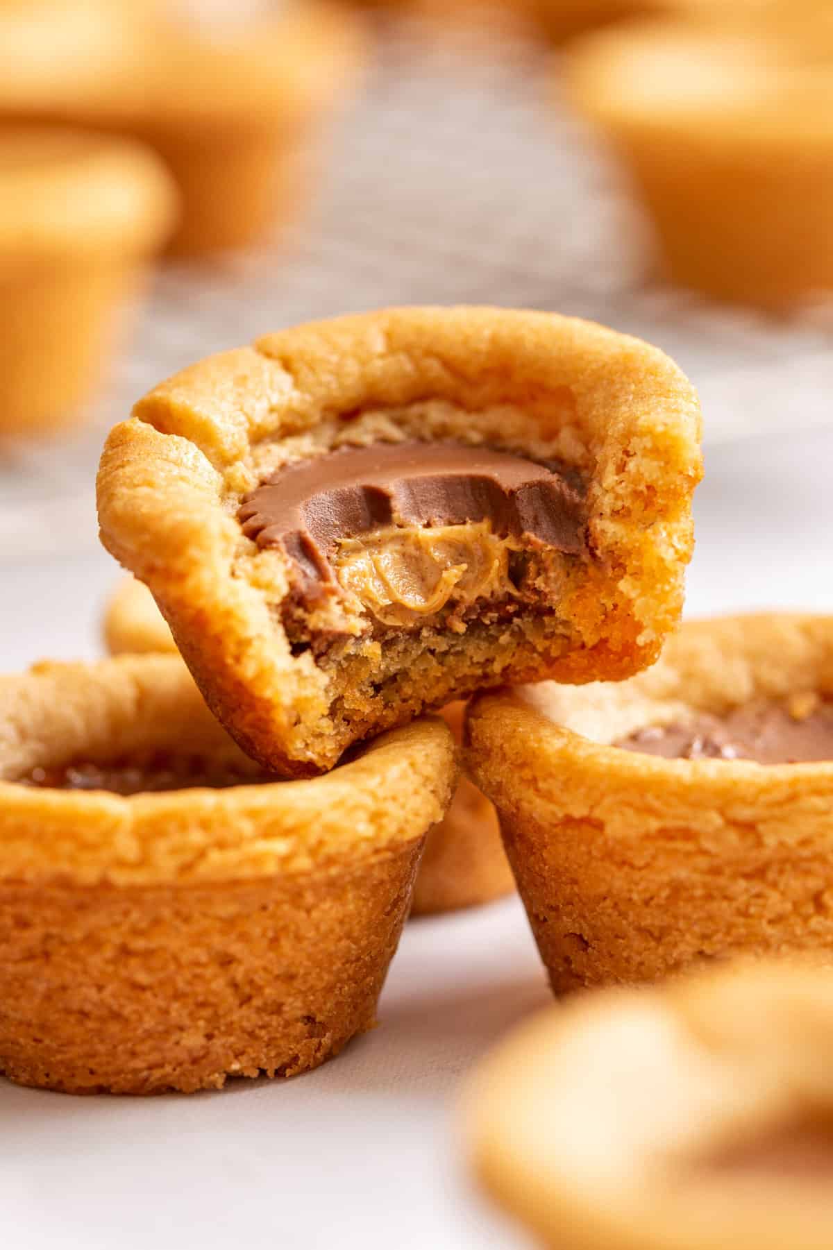 stack of peanut butter cookie cups sitting on a plate with one taken a bite out of. 