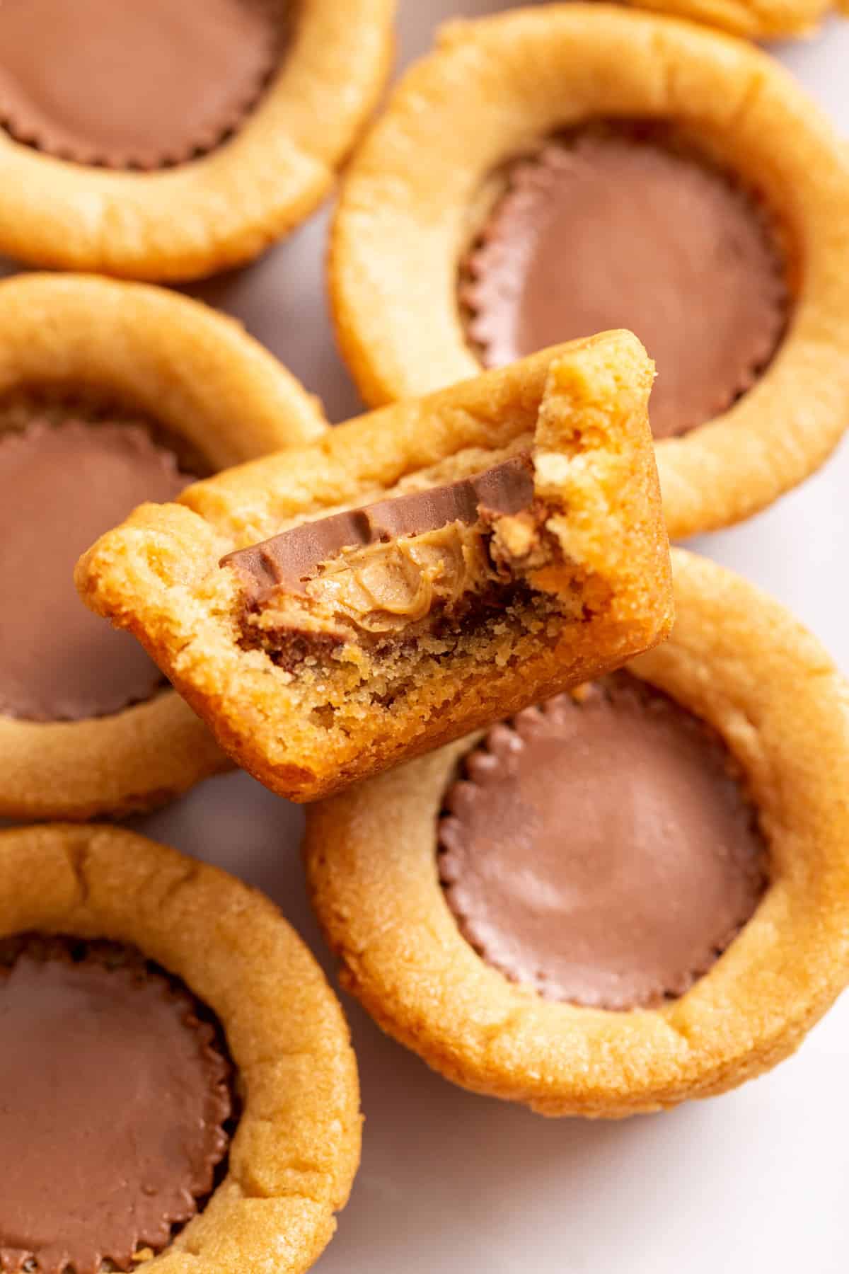 close up image of a bite taken out of a peanut butter cookie cup and sitting on a pile of cookie cups. 