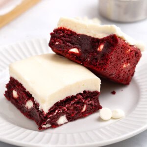 Two red velvet brownies with cream cheese frosting on a plate.