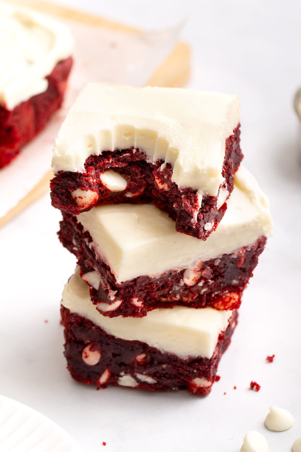 stack of three square sliced dense red velvet brownies with white chocolate chips and cream cheese frosting.