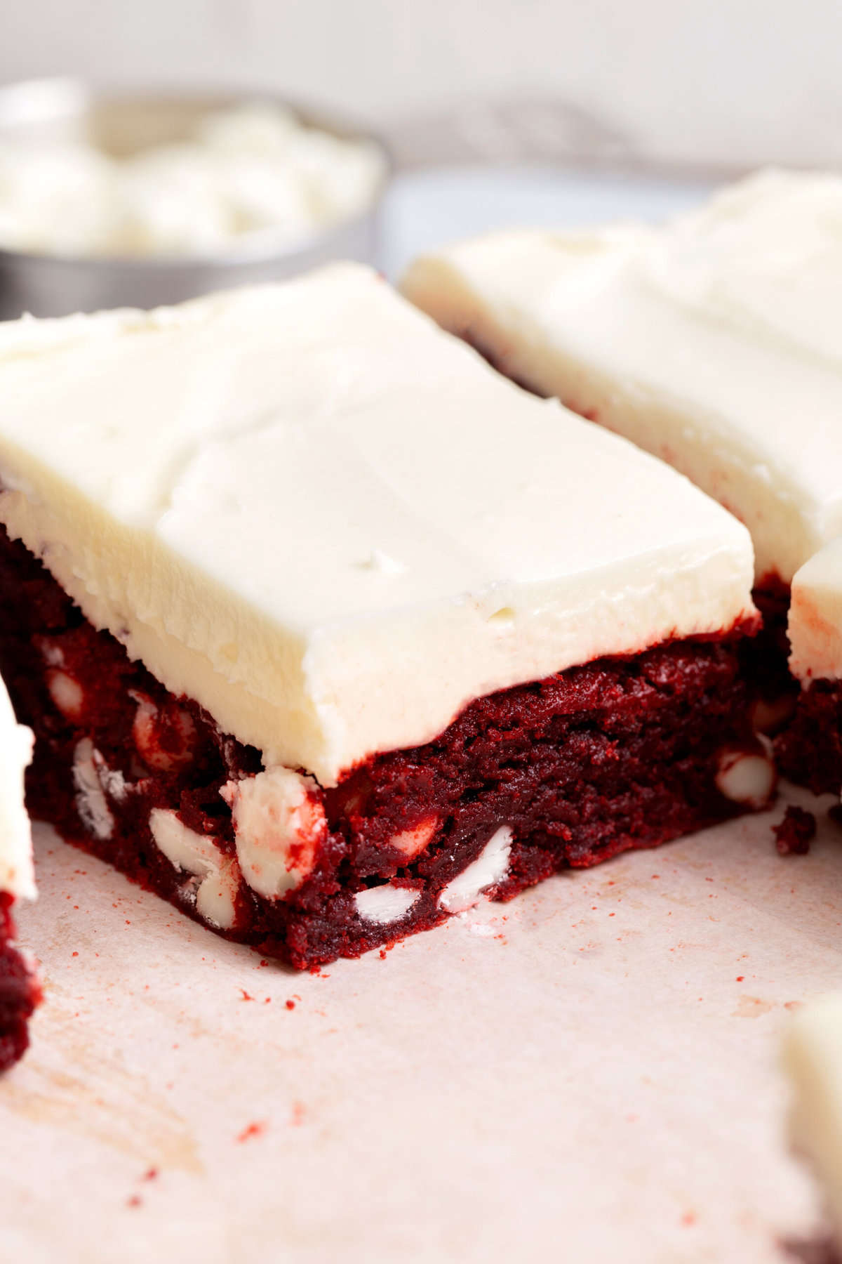close up image of the cross section of a square slice of red velvet brownies with white chocolate chips and cream cheese frosting.